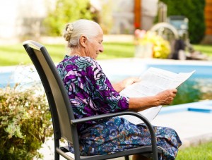 Elderly lady reading newspaper peacefully in her beautiful garden.