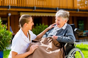 Nurse pushing senior woman in wheelchair on walk thru garden in summer